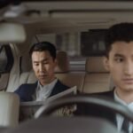 Elegant Asian businessman reading a newspaper inside a luxury car. Professional driver in focus