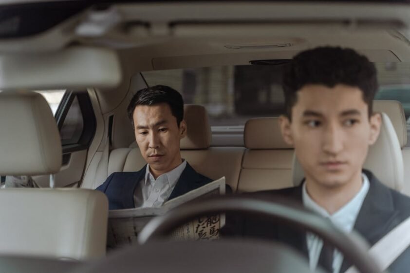 Elegant Asian businessman reading a newspaper inside a luxury car. Professional driver in focus